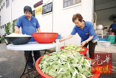 义工在厨房后部挑菜洗菜。